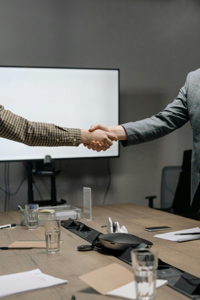 pexels-photo-6814524-6814524 Two business professionals shaking hands in a modern meeting room, symbolizing successful collaboration.